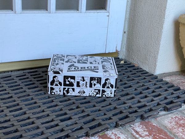 Forge Coffee Roasters Holiday Gift Box with drawn characters drinking coffee on the surfaces of the box, sitting on doorstep of a home.